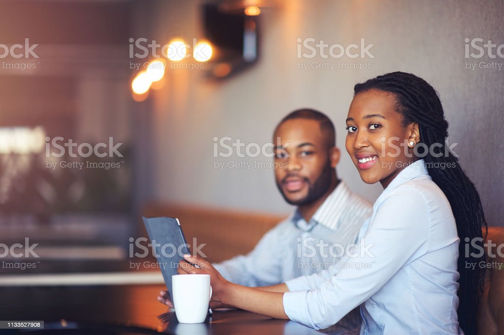 Young entrepreneurs planning together on a digital tablet having coffee looking at camera in Cape Town South Africa